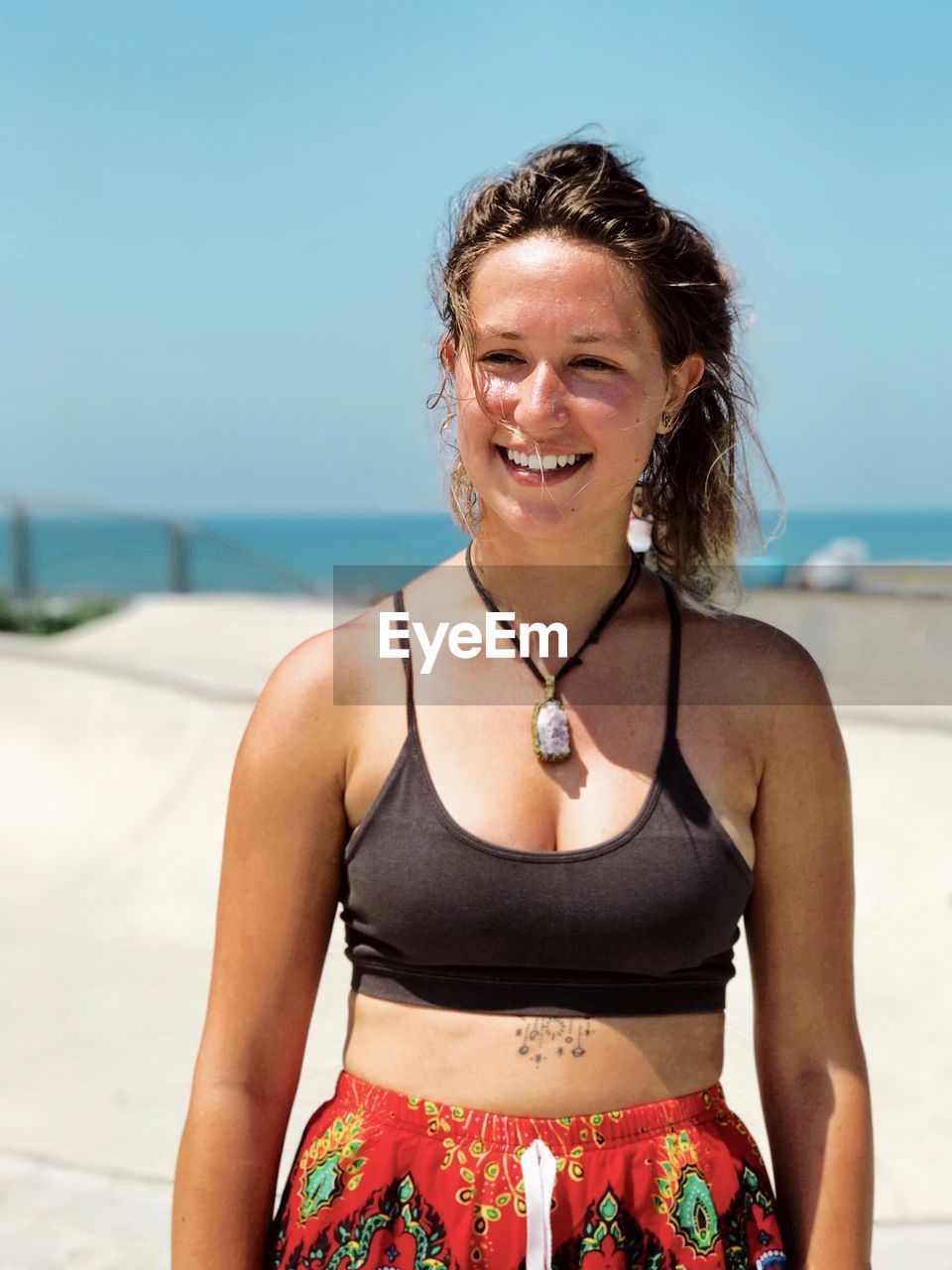 PORTRAIT OF YOUNG WOMAN STANDING AT BEACH