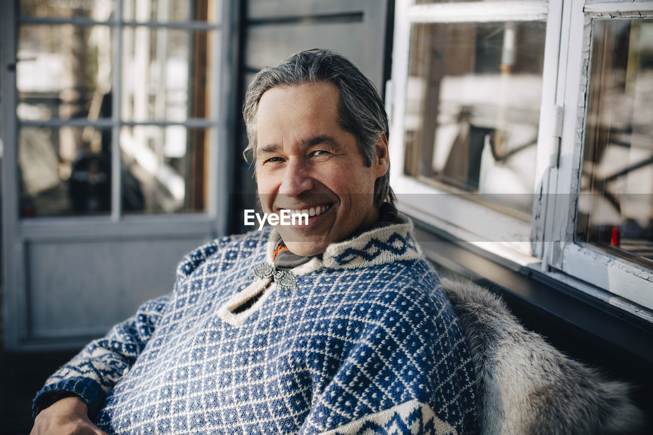 Cheerful mature man in warm clothing sitting at front porch