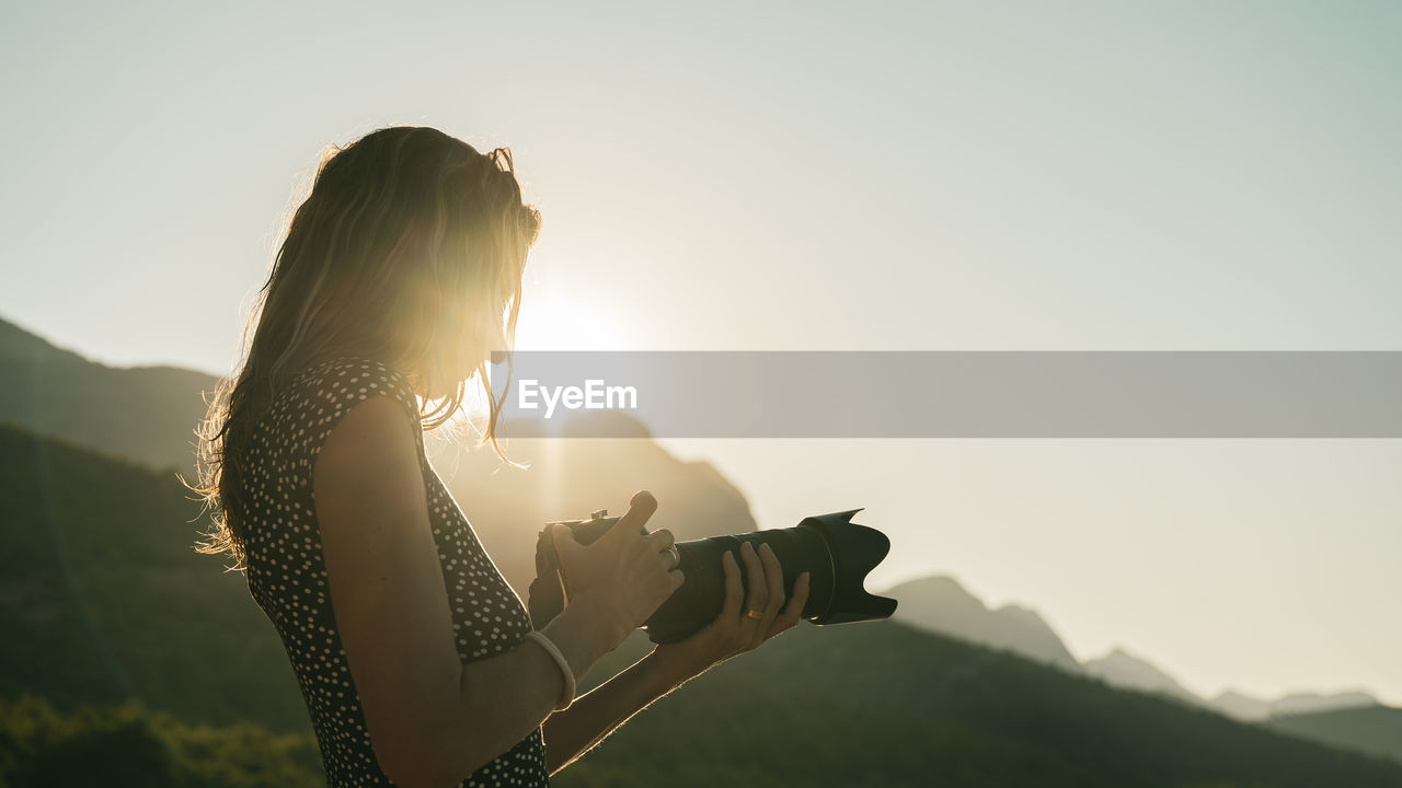 SIDE VIEW OF WOMAN HOLDING UMBRELLA AGAINST SKY