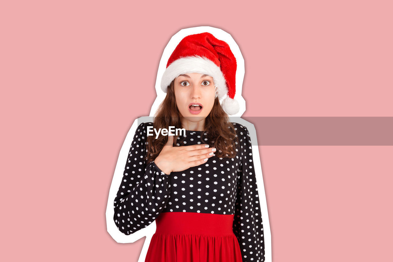 Surprised young woman wearing santa hat against colored background