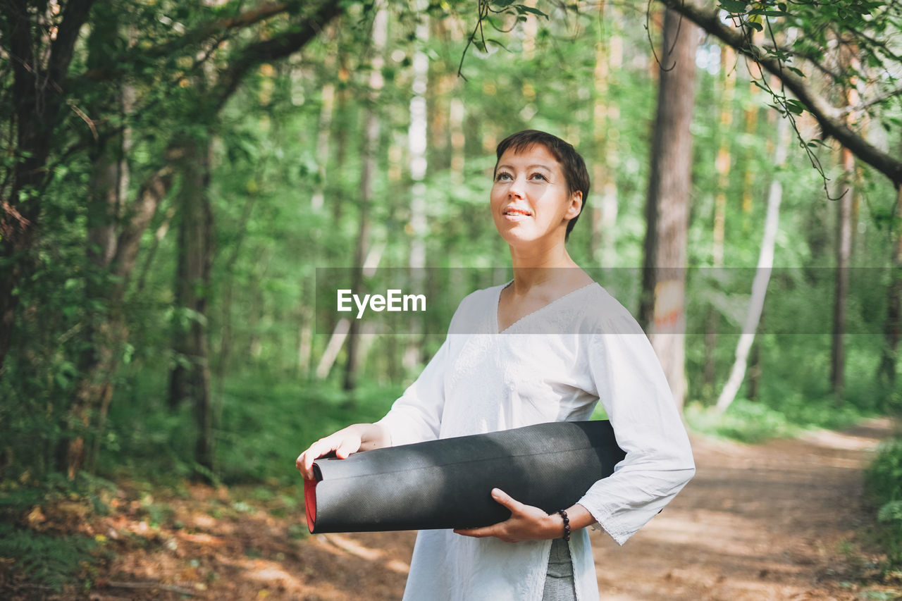 Smiling young woman standing by trees in forest