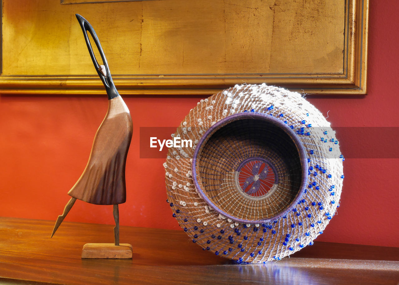 Carved wooden woman figurine standing next to beaded woven basket.