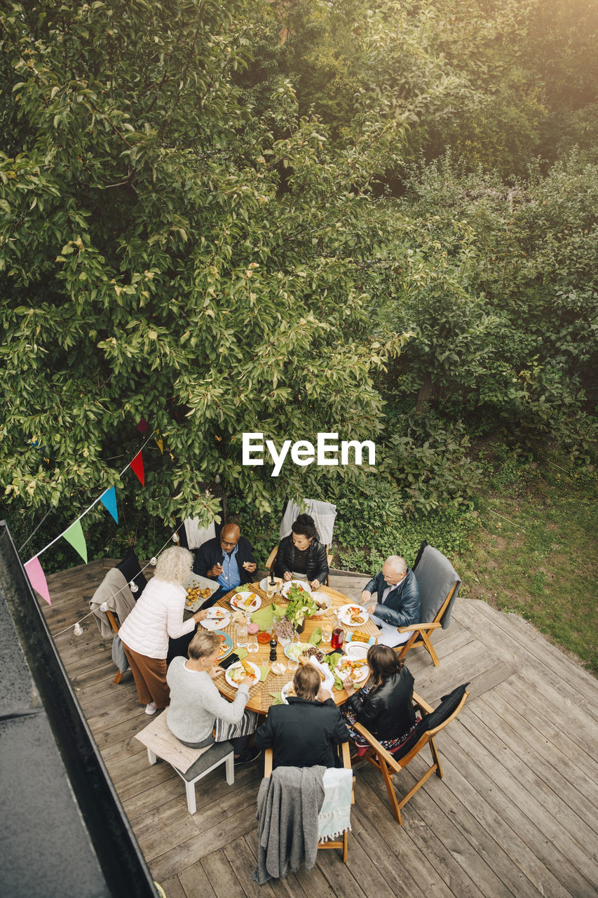 High angle view of senior woman serving friends sitting at dining table during garden party in back yard