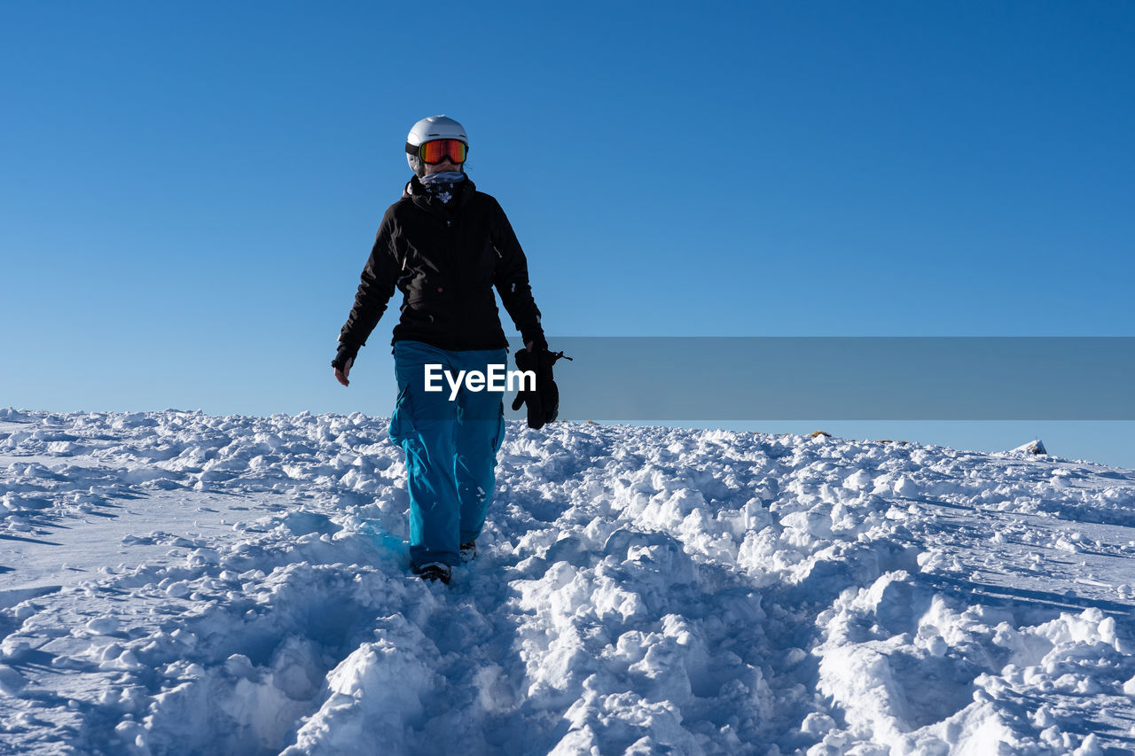 Woman standing by snowcapped mountain against blue sky