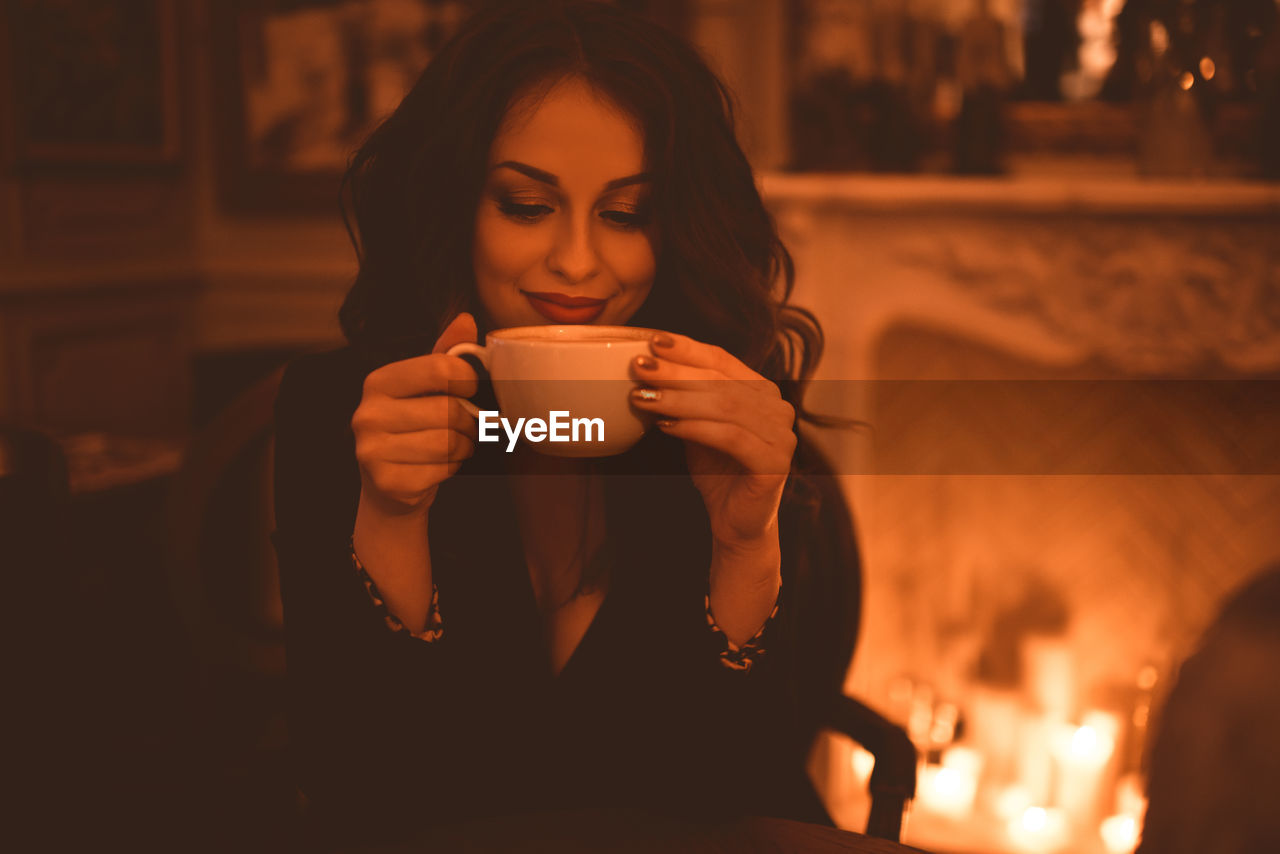 Smiling beautiful woman sipping fresh coffee in cafe closeup over burning candles. good evening