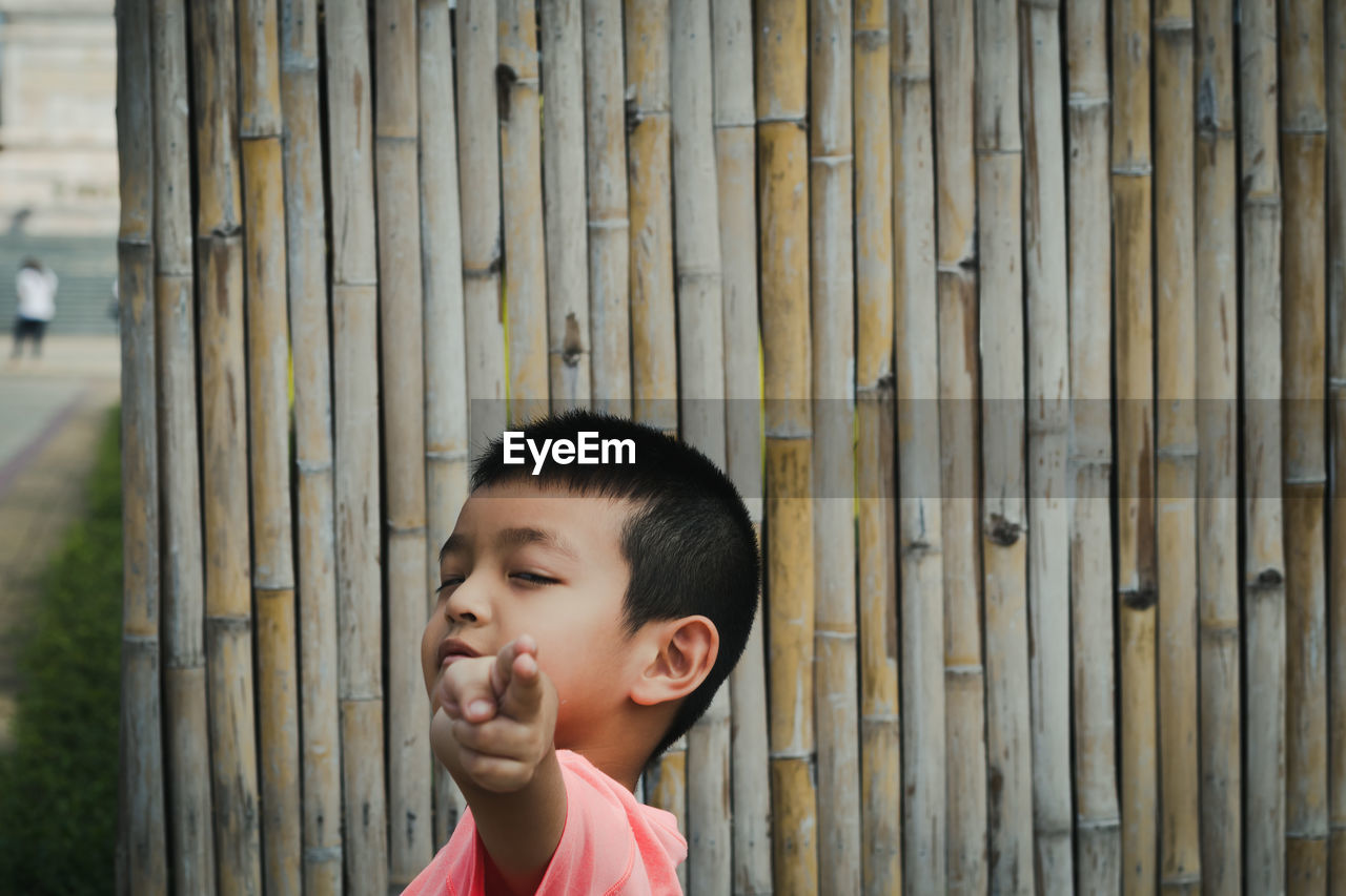Portrait of cute boy gesturing against bamboo fence