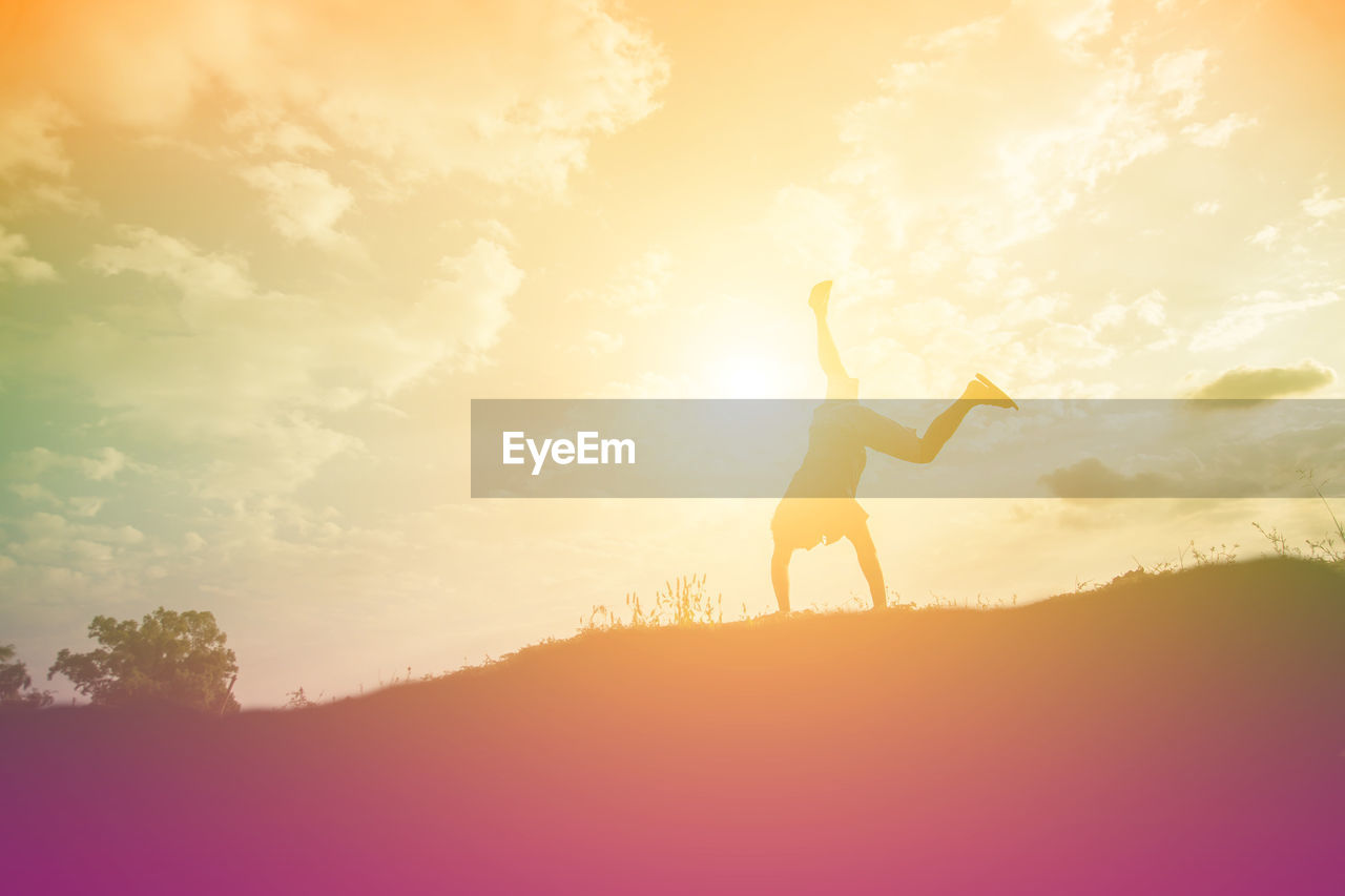 Silhouette man doing handstand on mountain against sky during sunset