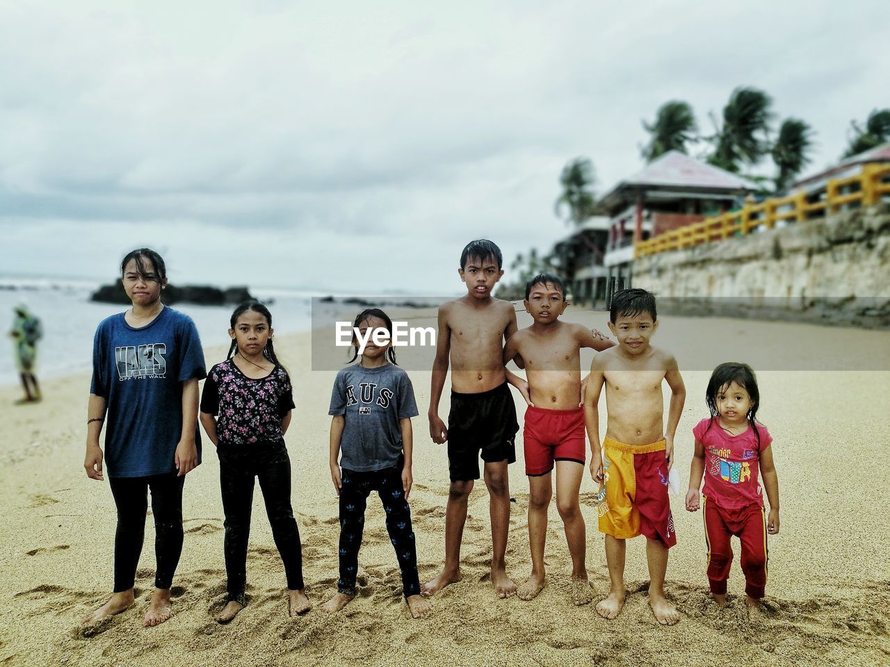 FULL LENGTH PORTRAIT OF FRIENDS STANDING ON BEACH AGAINST SKY