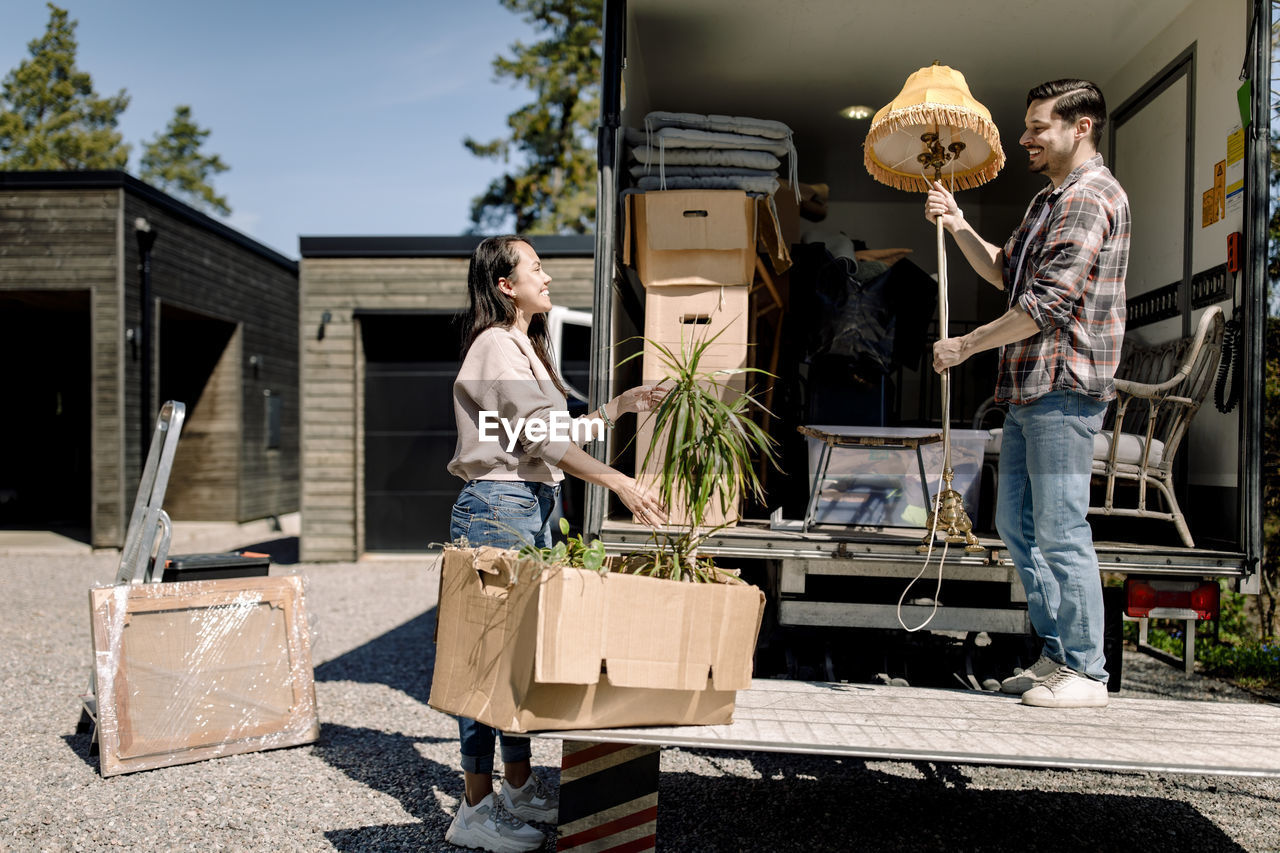 Couple unloading cardboard boxes from truck during sunny day