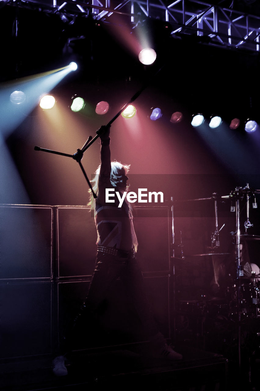 Man carrying microphone stand while standing on stage at concert