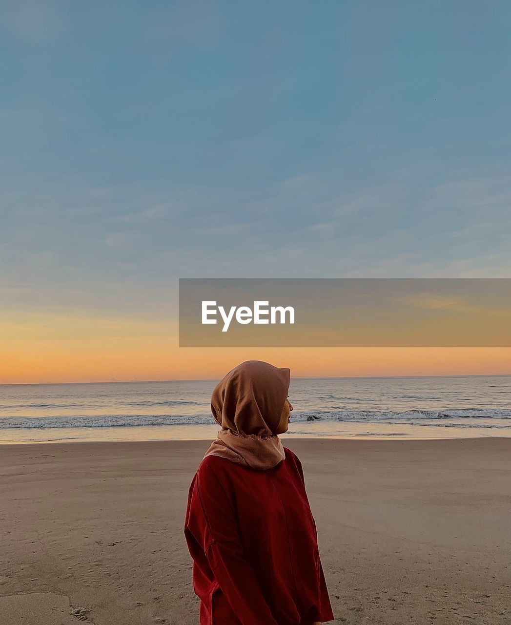 Rear view of woman looking at sea against sky during sunset