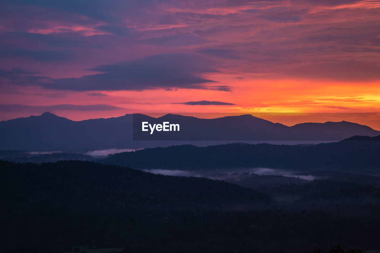 Mountains range misty shadow with dramatic colorful sunset sky at dusk from flat angle