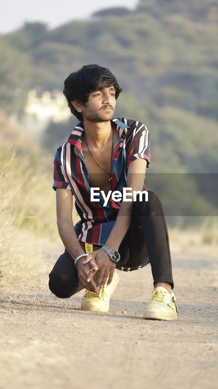 Young man looking away while sitting on land