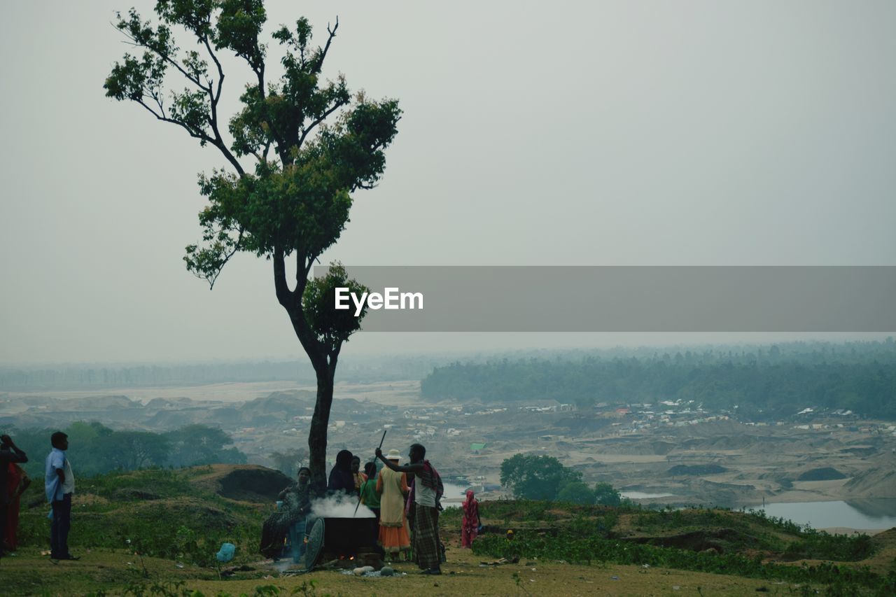 PEOPLE STANDING ON TREE AGAINST SKY