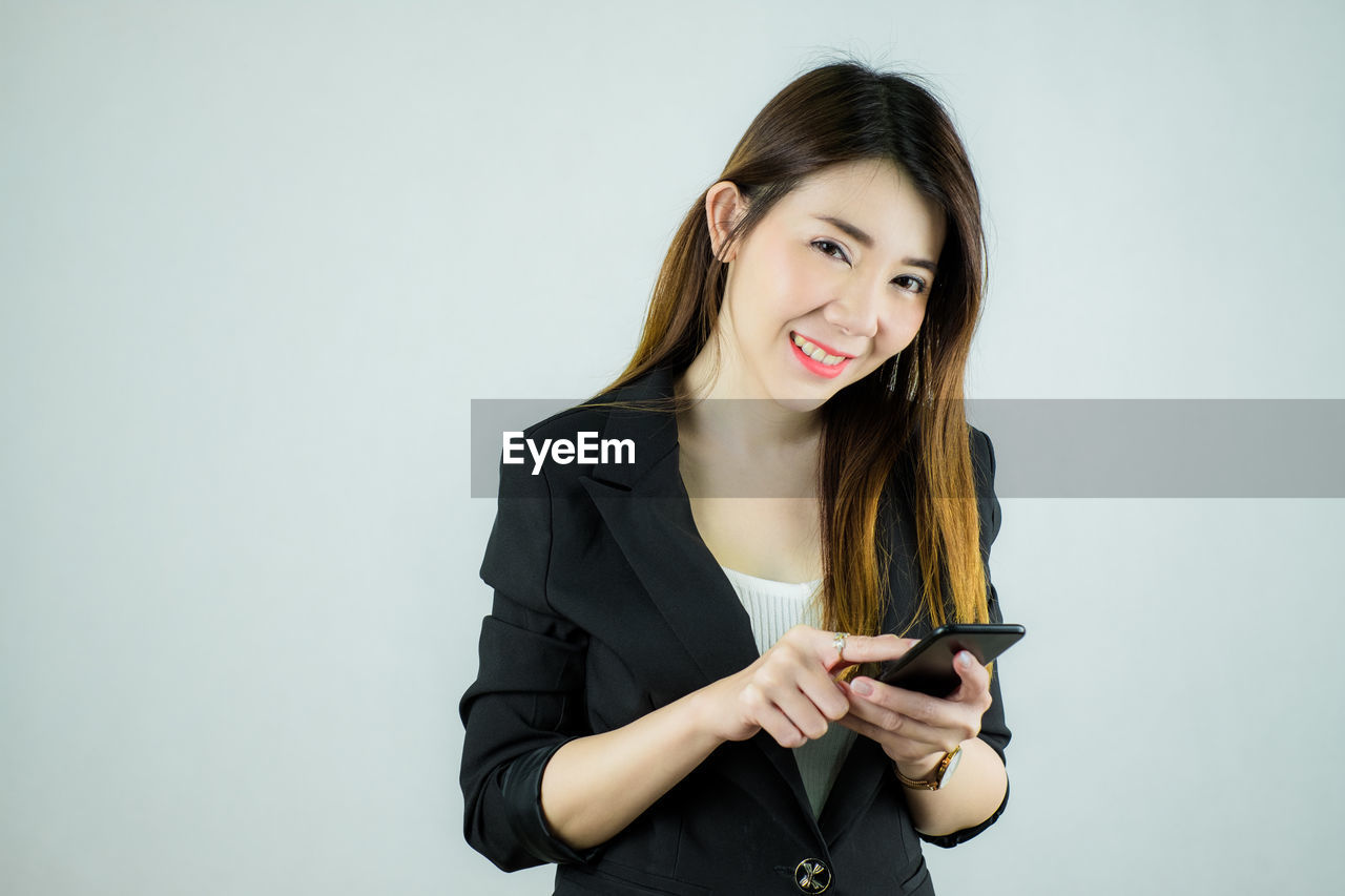 PORTRAIT OF YOUNG WOMAN USING PHONE AGAINST WHITE BACKGROUND