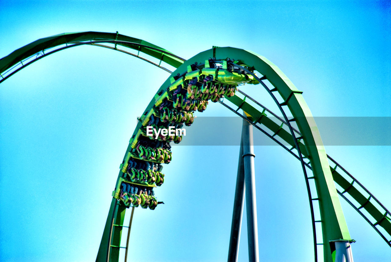 Low angle view of people enjoying rollercoaster against blue sky