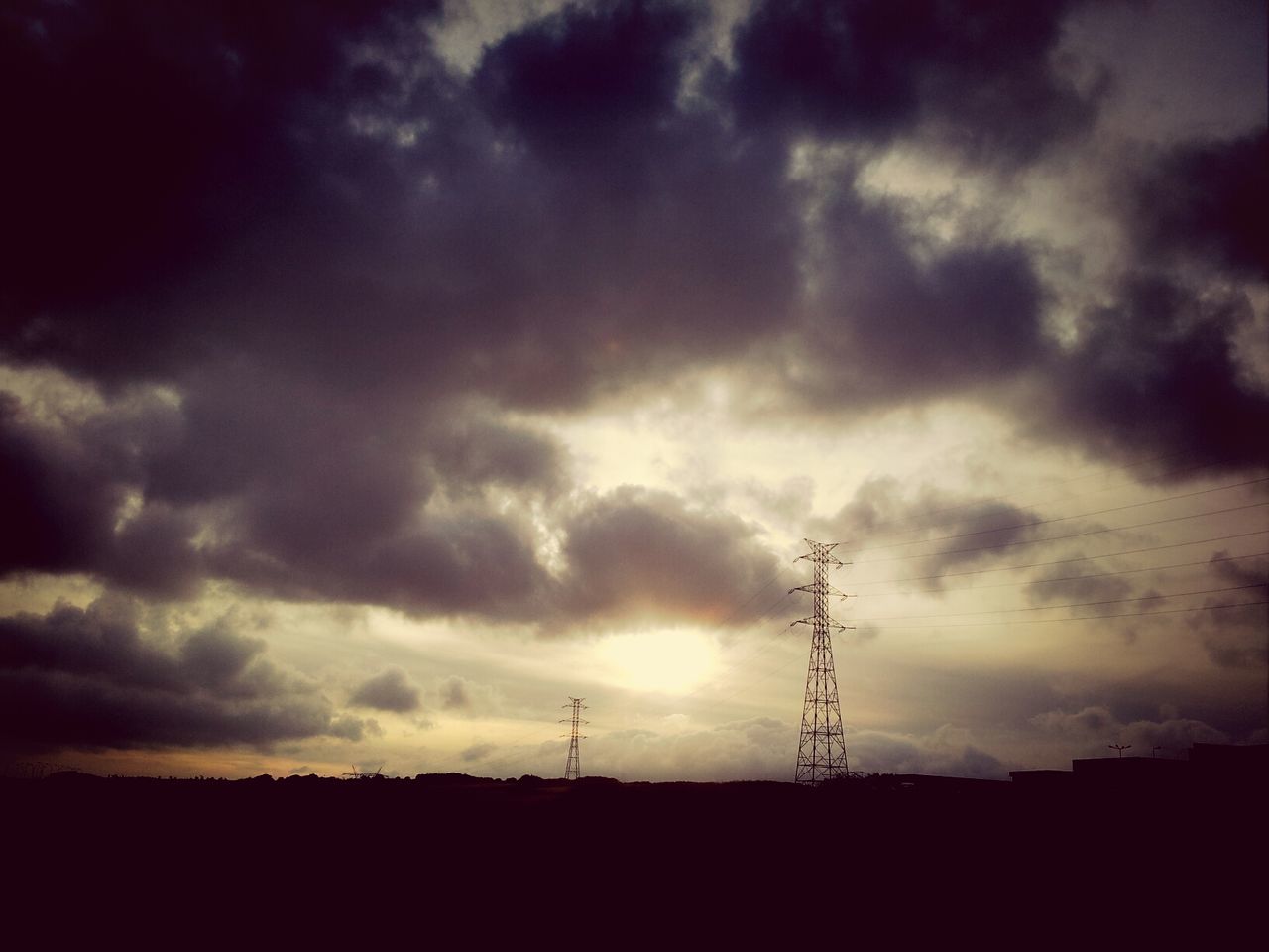 Silhouette electricity pylons against dramatic sky