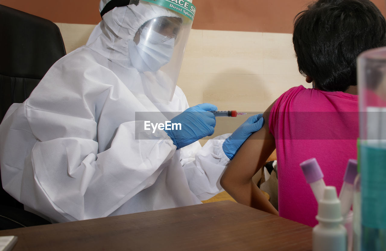 Doctor wearing protective suit giving vaccine to girl