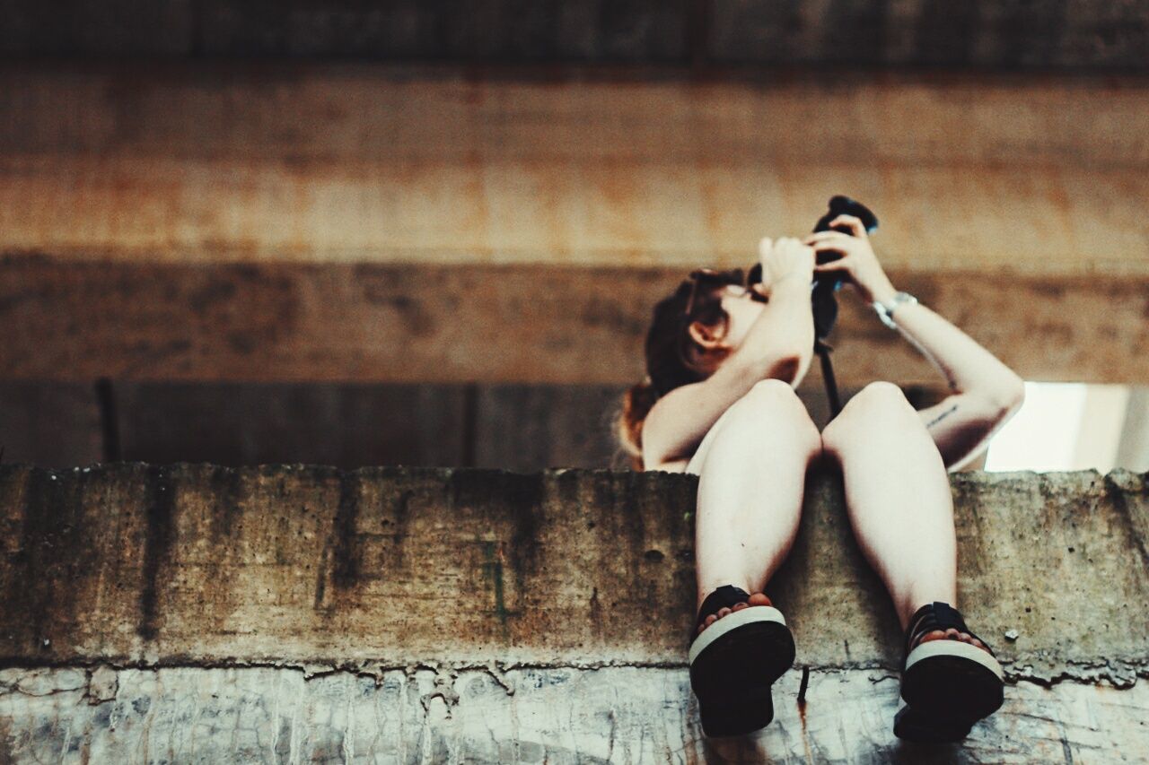 Full length of woman photographing while sitting on retaining wall