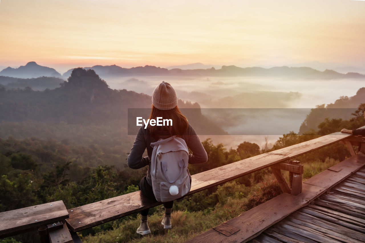 REAR VIEW OF MAN STANDING ON MOUNTAIN ROAD AGAINST SKY