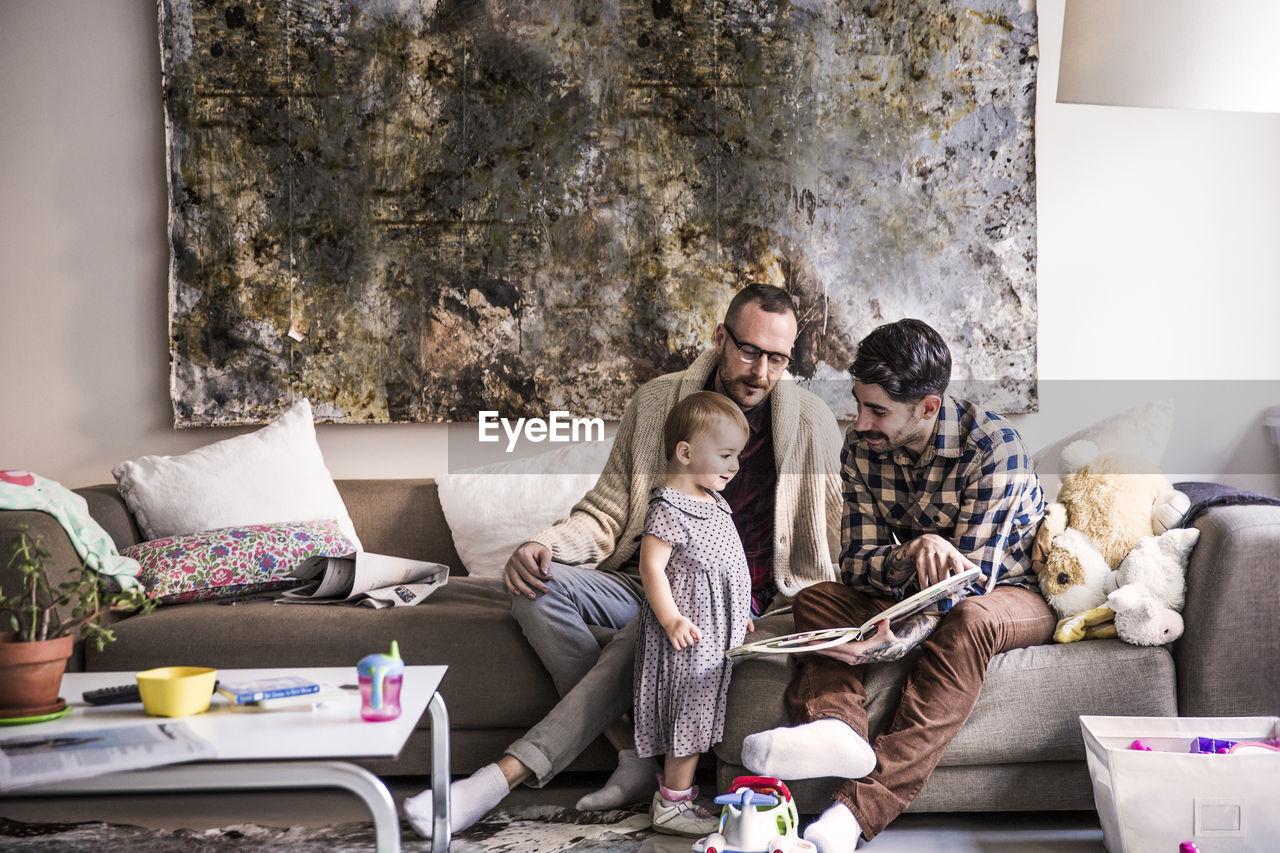 Fathers reading book to daughter while sitting on sofa at home