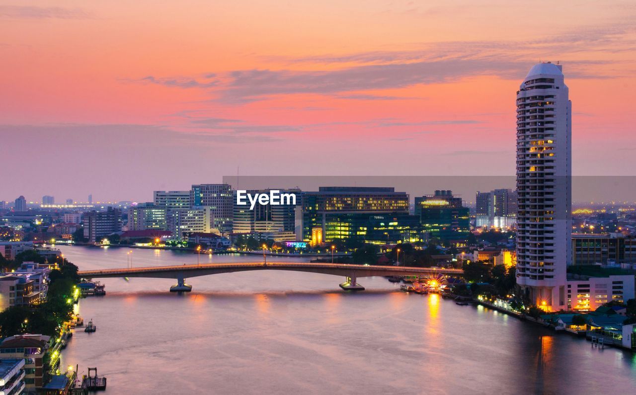 Phra pin-klao bridge over chao phraya river amidst illuminated cityscape at dusk