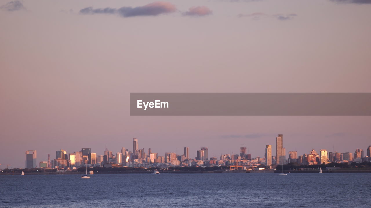 Sea by buildings against sky during sunset