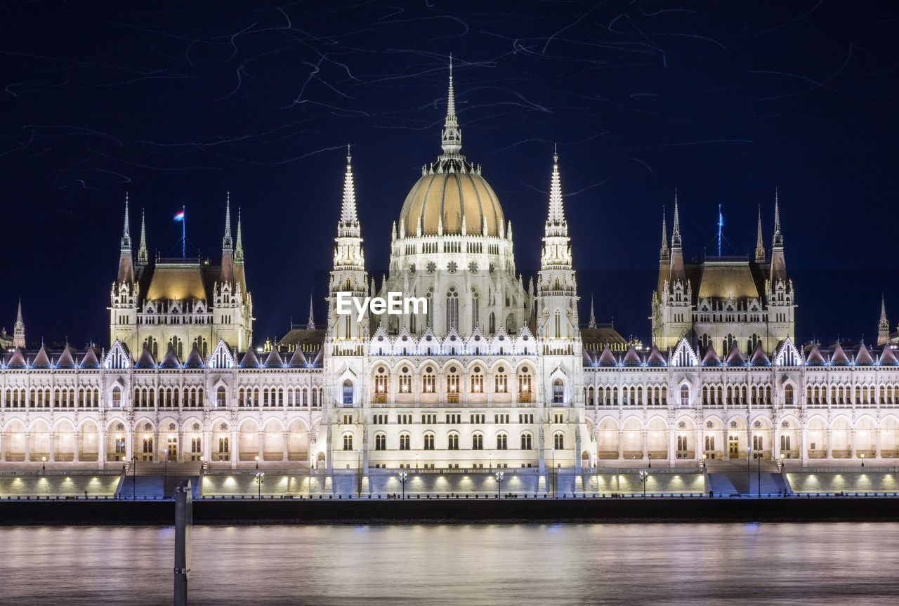 Illuminated hungarian parliament building by river against sky at night