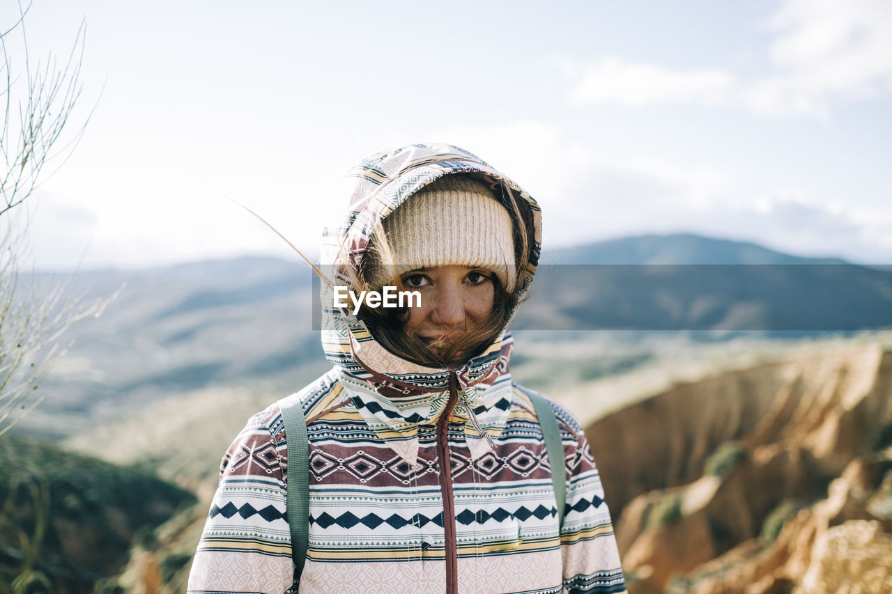 Young tourist in warm clothes looking at camera against mounts during trip in spain