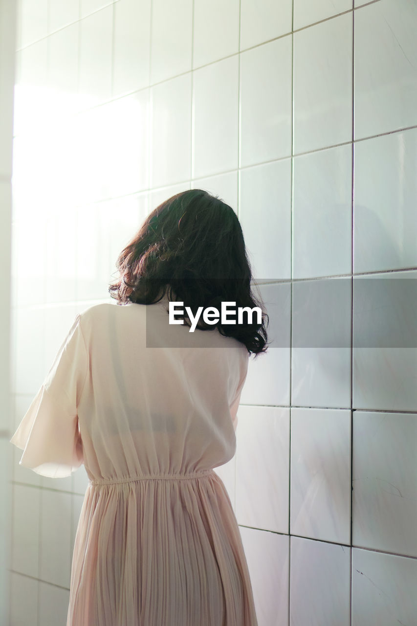 Rear view of woman standing in bathroom at home