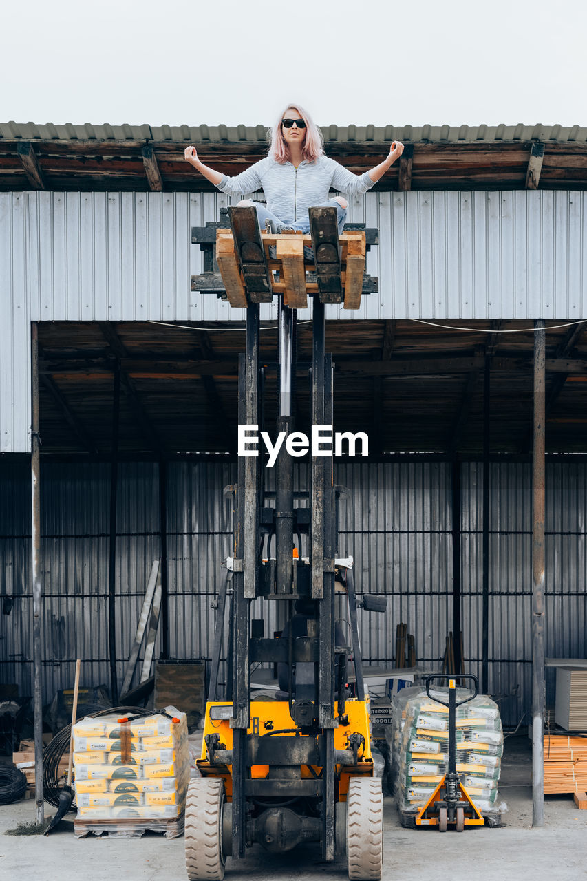 Woman standing on forklift in front of built structure
