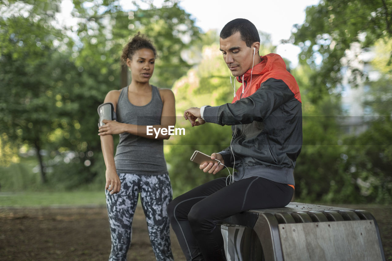 Man looking at wristwatch while woman touching arm band