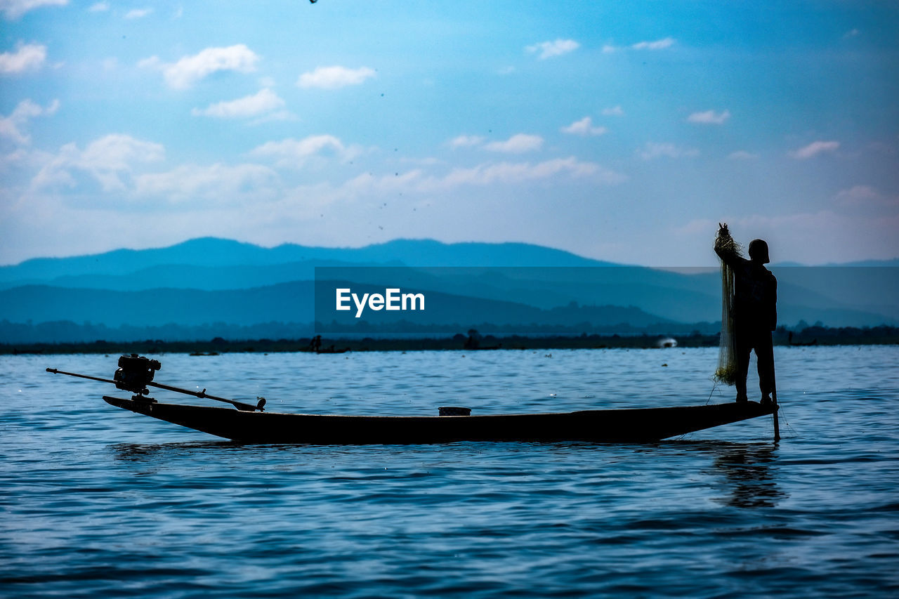 Silhouette man on boat in inlay lake against sky