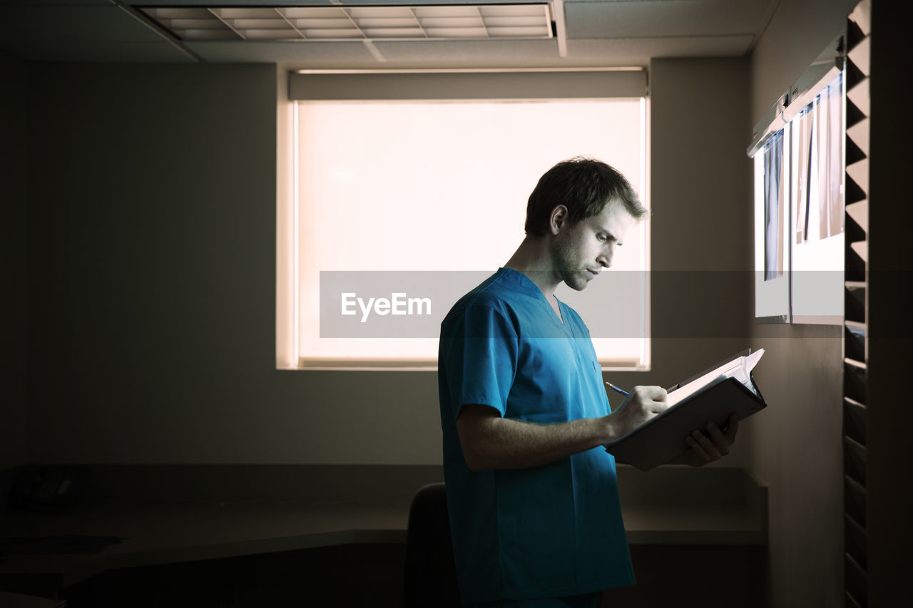 Doctor writing report while standing in hospital ward