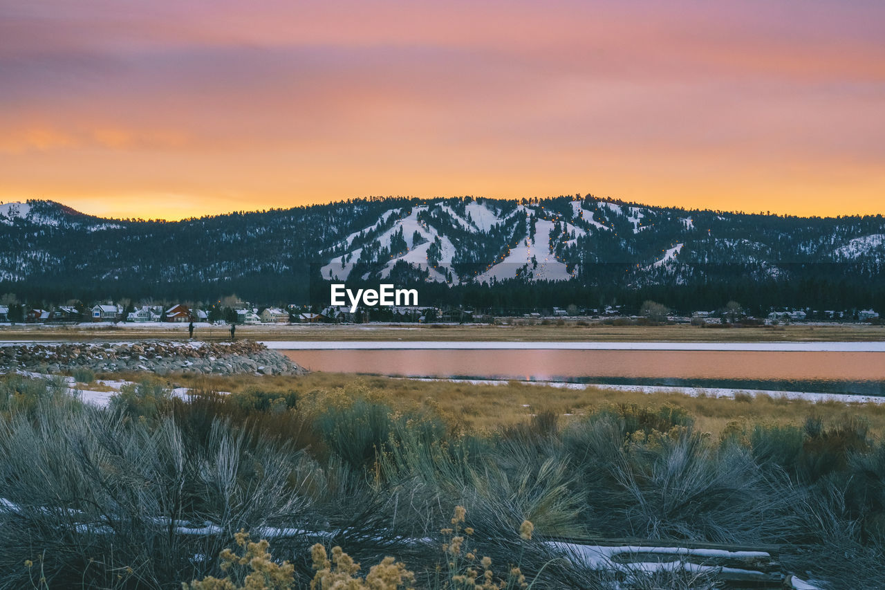 Scenic view of lake amd snowcapped mountains against cloudy sky during sunset