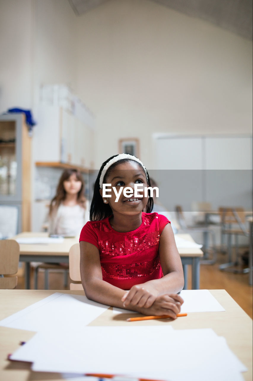 Smiling girl listening while sitting at desk in classroom