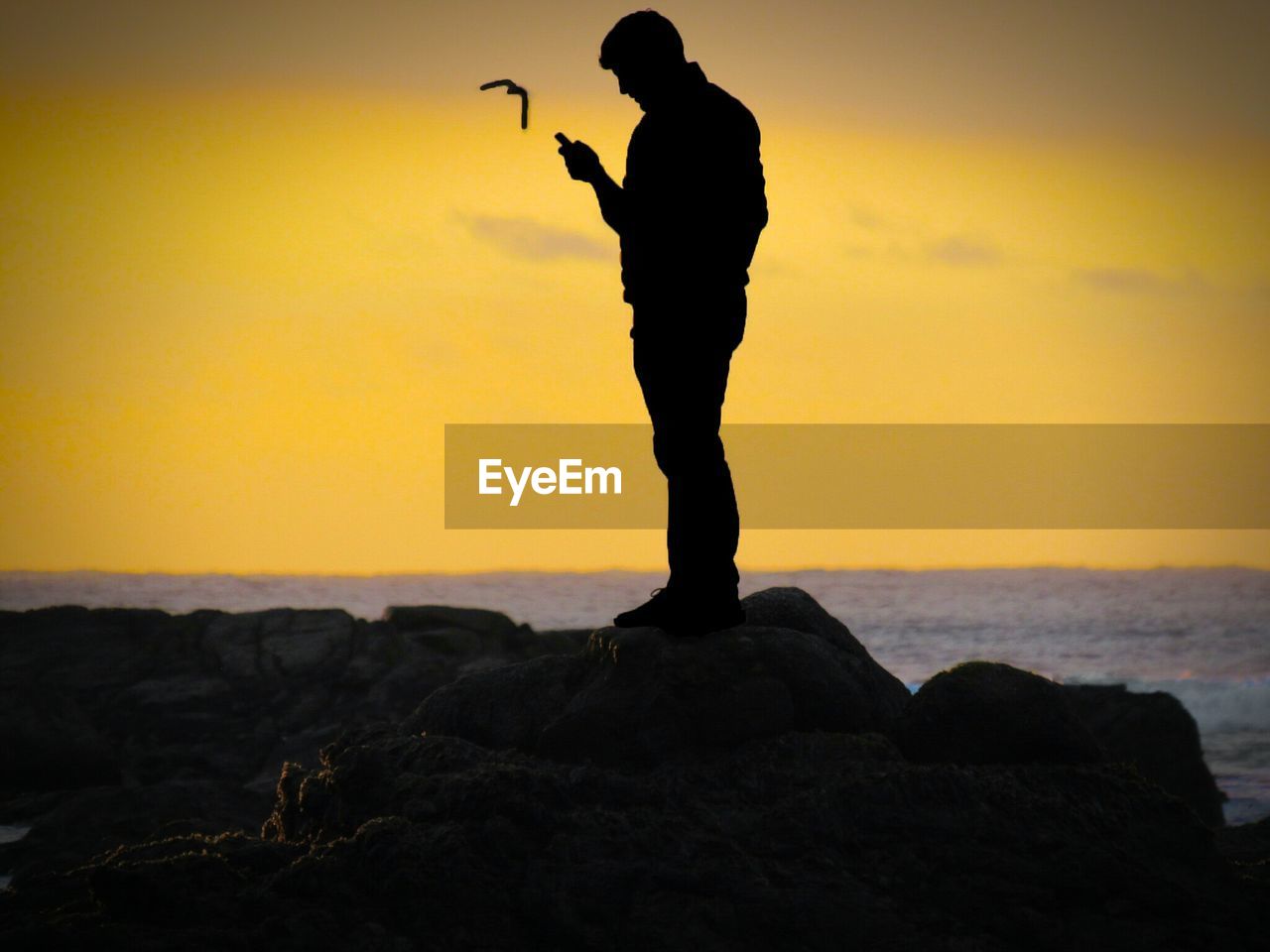 Silhouette man standing on rock at beach during sunset