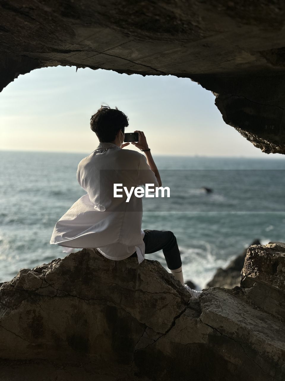 rear view of man sitting on rock at beach