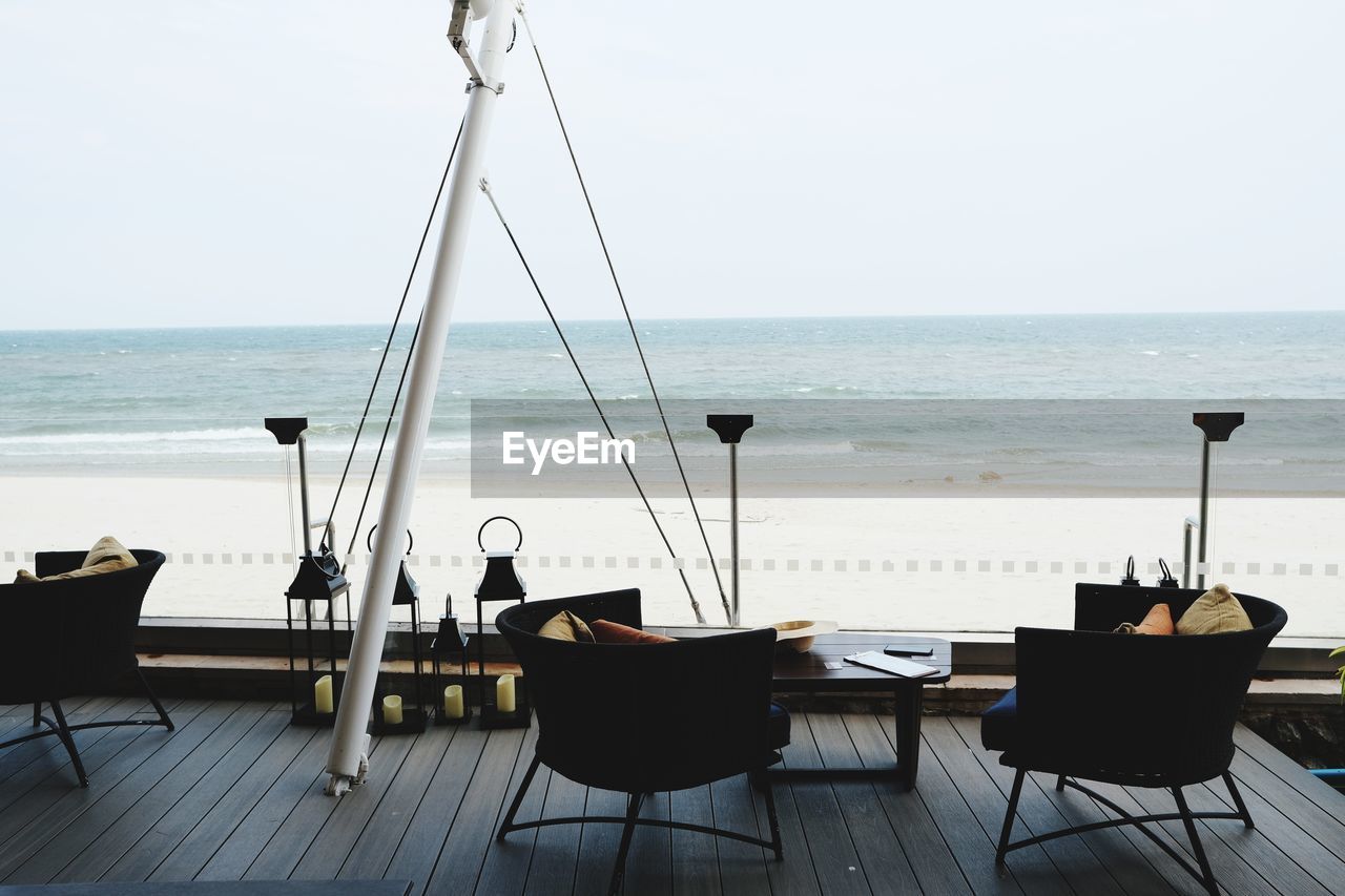 Chairs and table on beach against clear sky