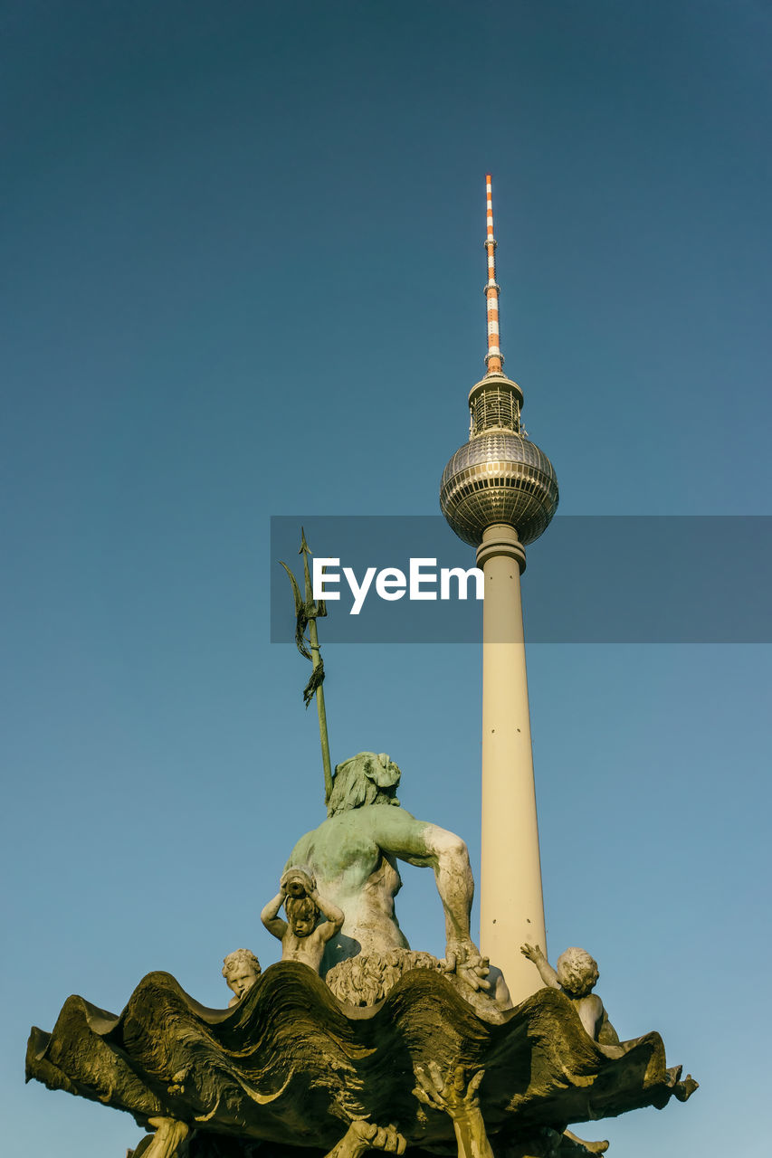 Low angle view of statues and fernsehturm against clear blue sky