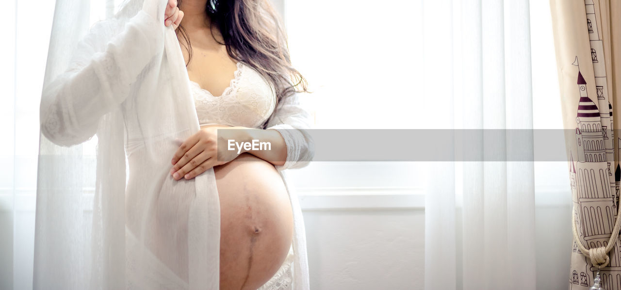 MIDSECTION OF WOMAN SITTING AT WINDOW