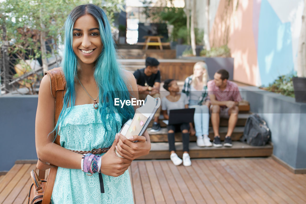 Portrait of young woman holding book with friends in background