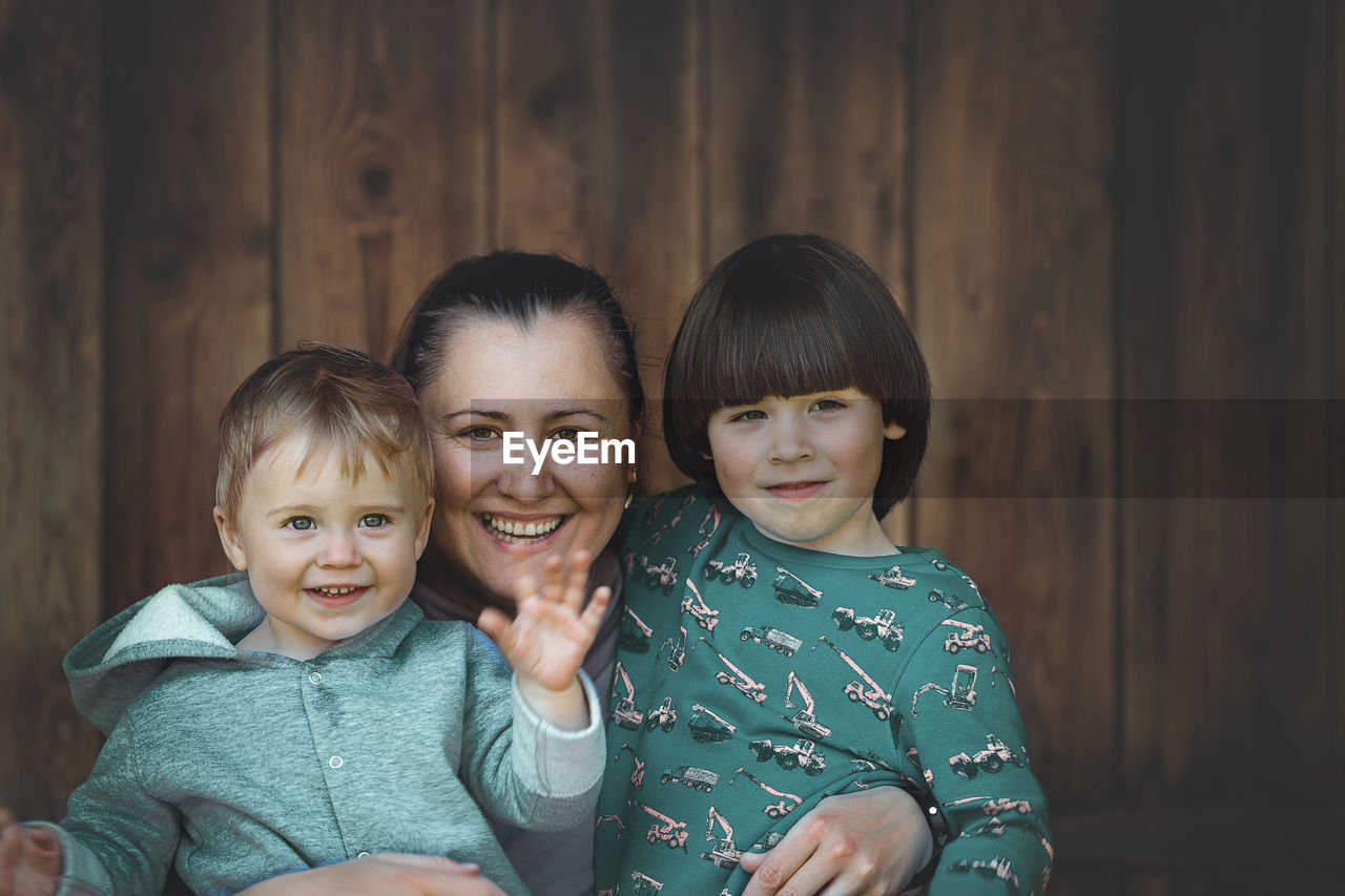 Portrait of smiling mother with kids against wooden wall