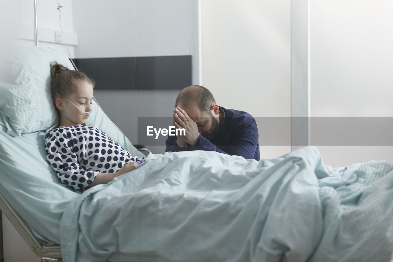 Worried man sitting by daughter's bed in hospital ward