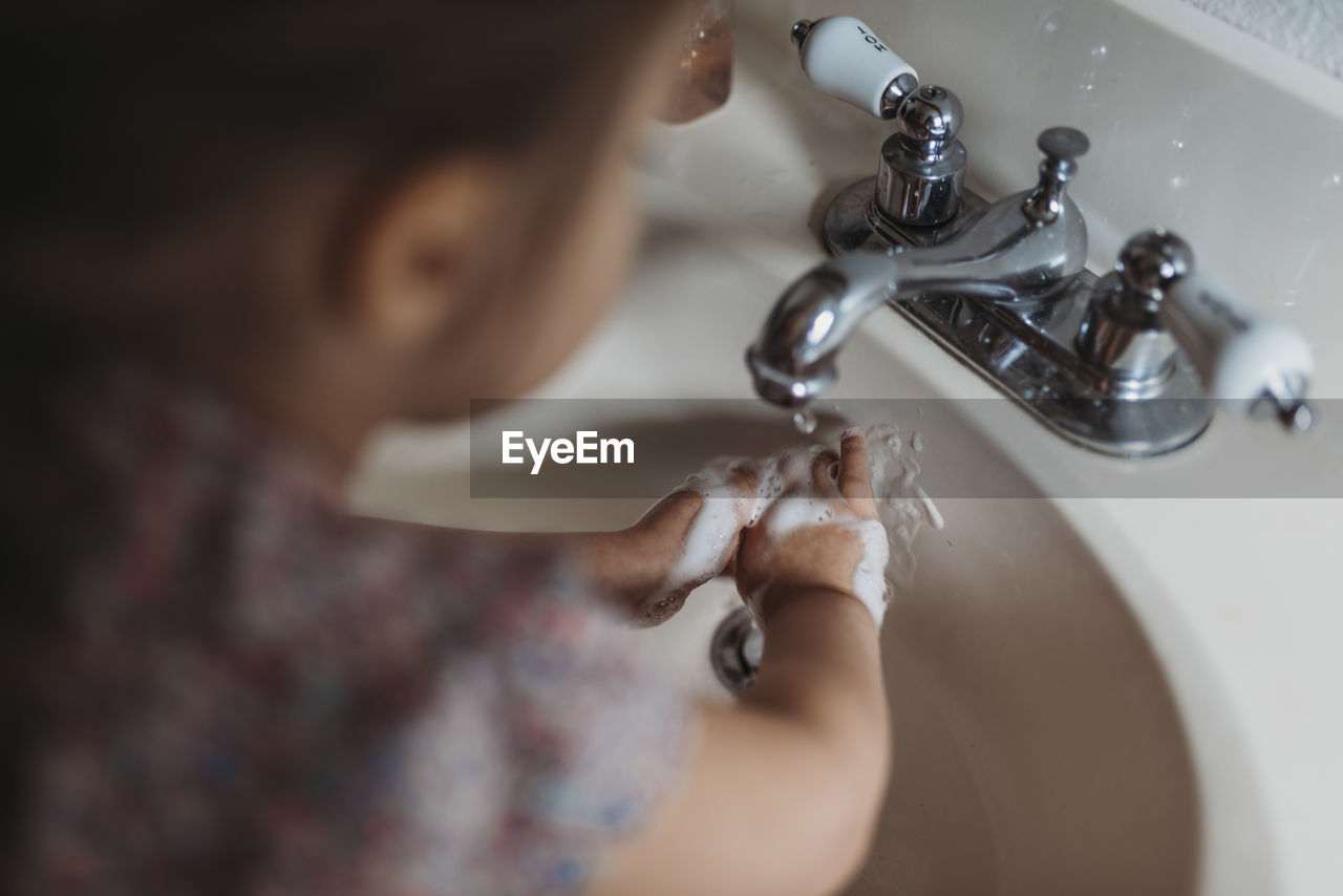 Young preschool aged girl washing hands in sink with soap