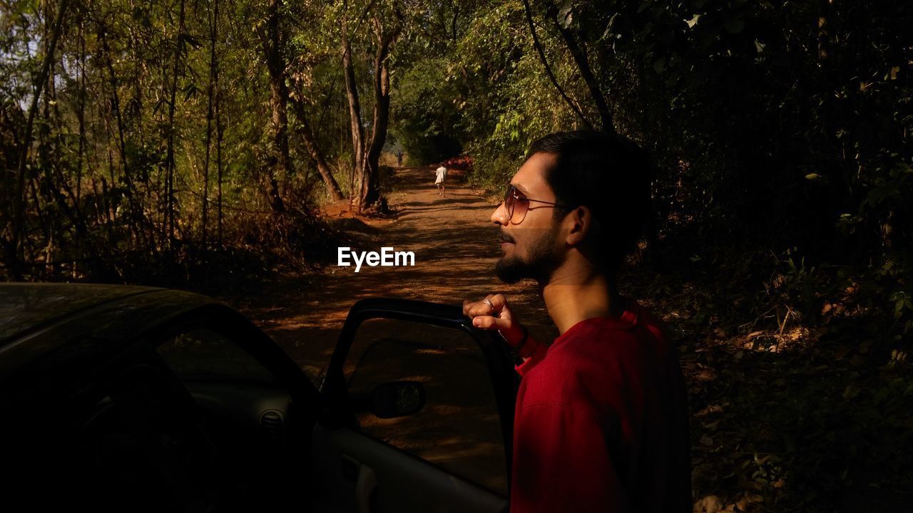 Profile view of man standing with car in forest