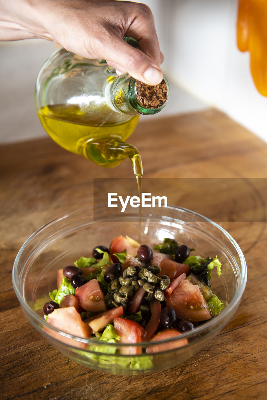 Close up of woman hands pouring olive oil over a salad.
