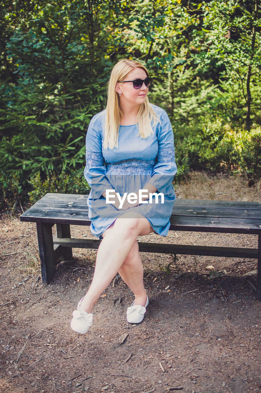 Young woman in sunglasses sitting on bench against plants