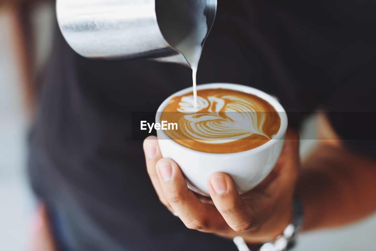 Close-up of hand pouring milk in coffee cup