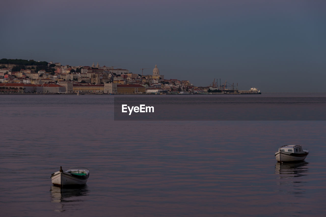 SAILBOATS IN SEA AGAINST BUILDINGS IN CITY AGAINST CLEAR SKY